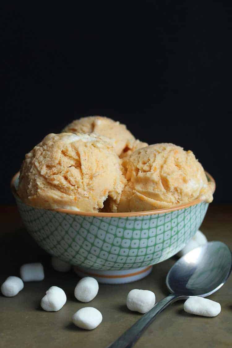A bowl of sweet potato ice cream scoops with spoon and marshmallows in background