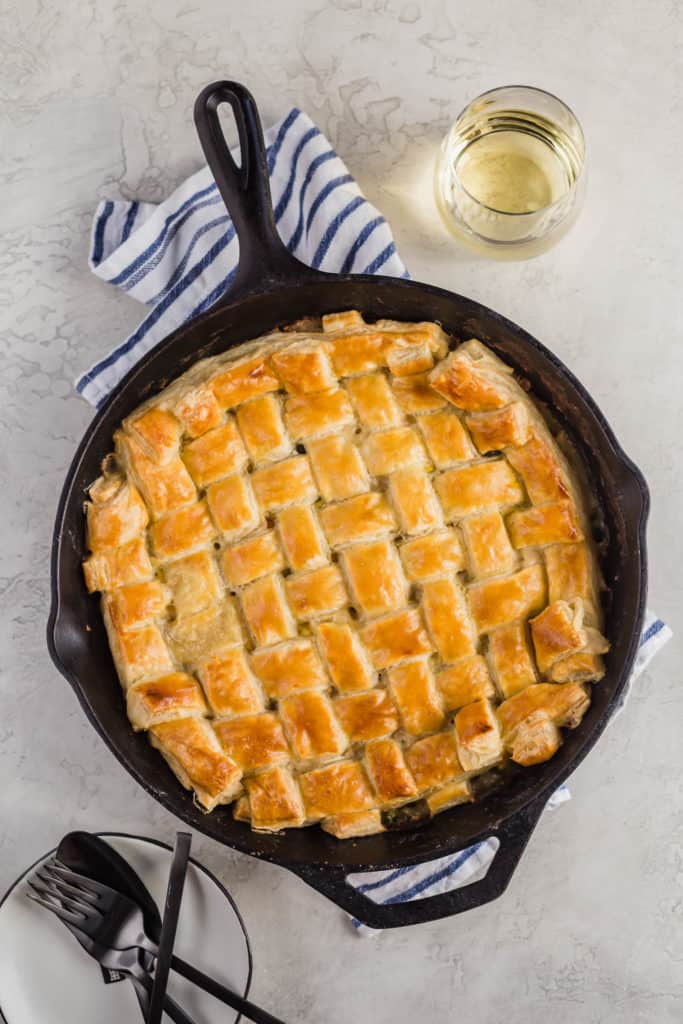 An overhead of an easy chicken pot pie with a lattice puff pastry crust with a glass of wine