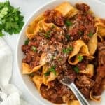 Beef ragu being served on a white plate with fork serving some on white background