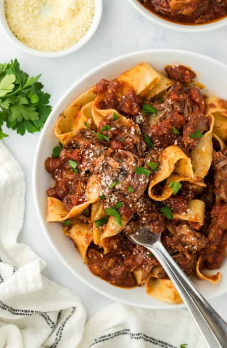 Beef ragu being served on a white plate with fork serving some on white background