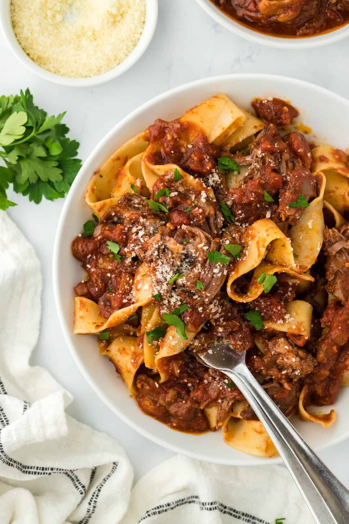 A bowl of short rib ragu being twirled with a silver fork in white bowl on white background