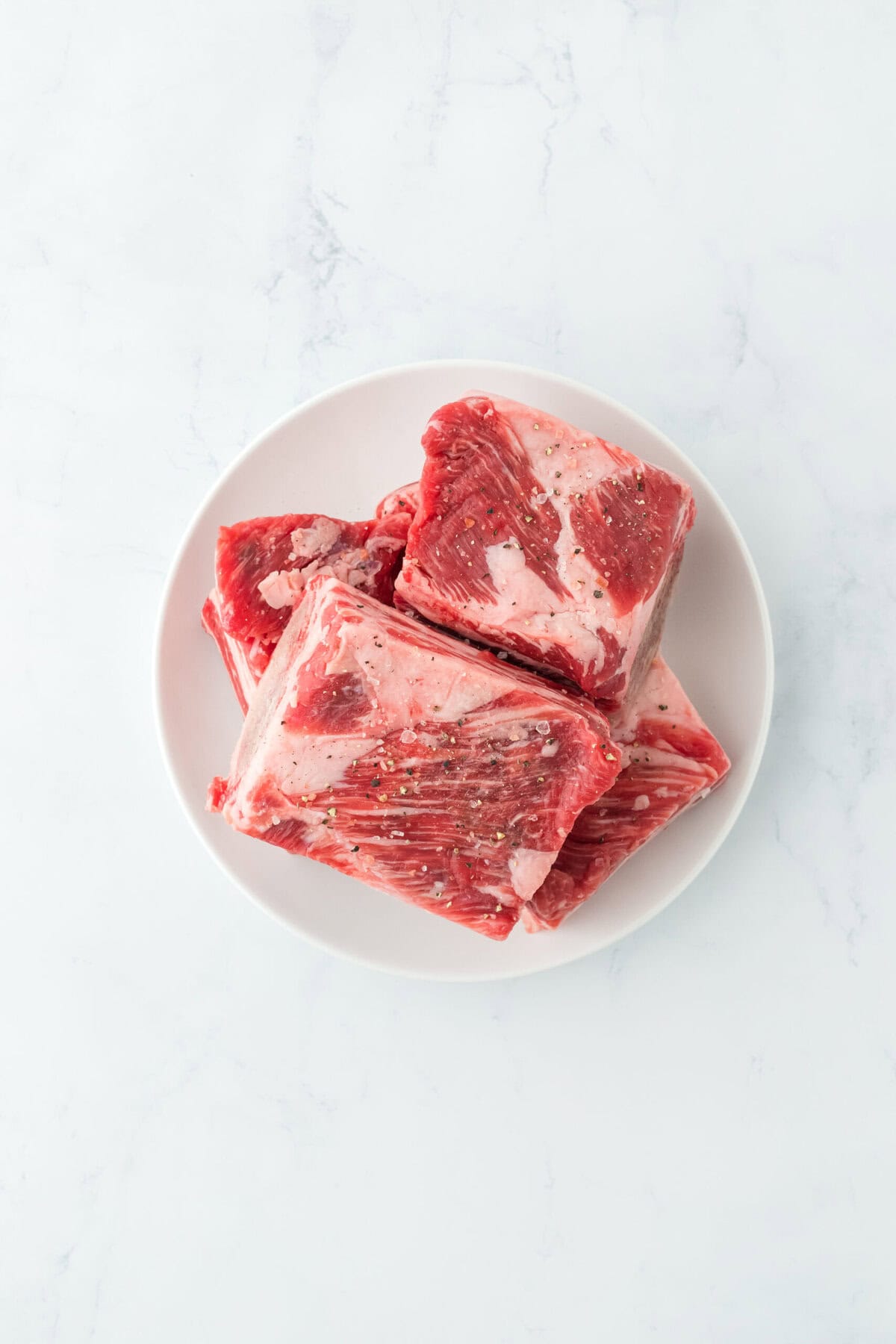 Seasoned short ribs on a white plate on white countertop