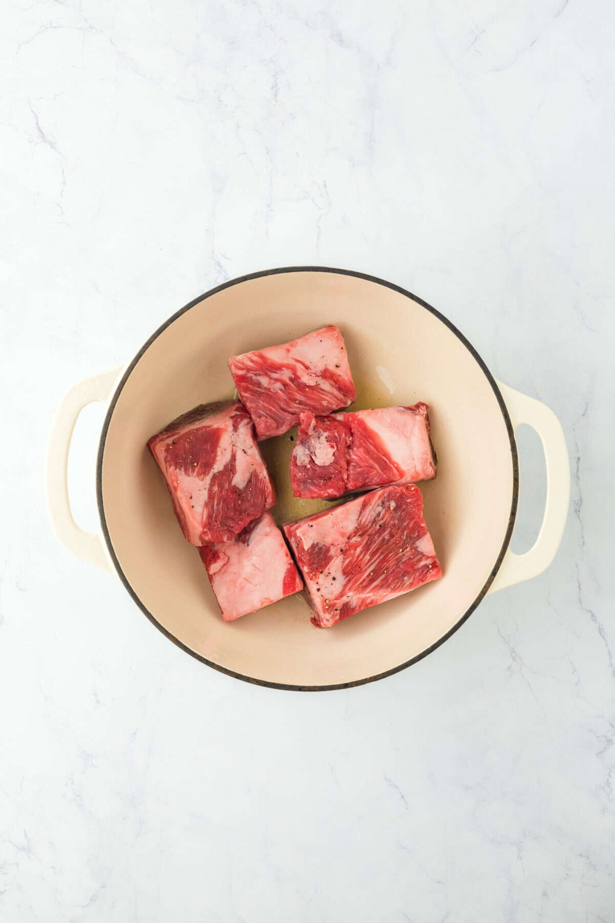 Short ribs searing in a dutch oven on white countertop