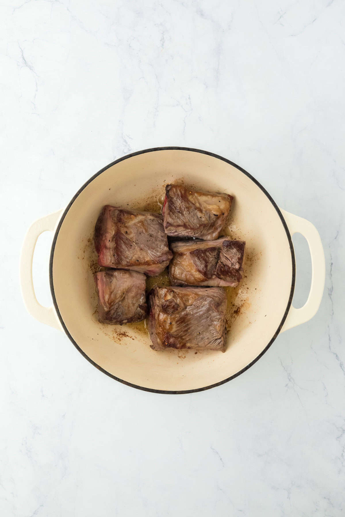 Short ribs browning in a hot pot on white countertop