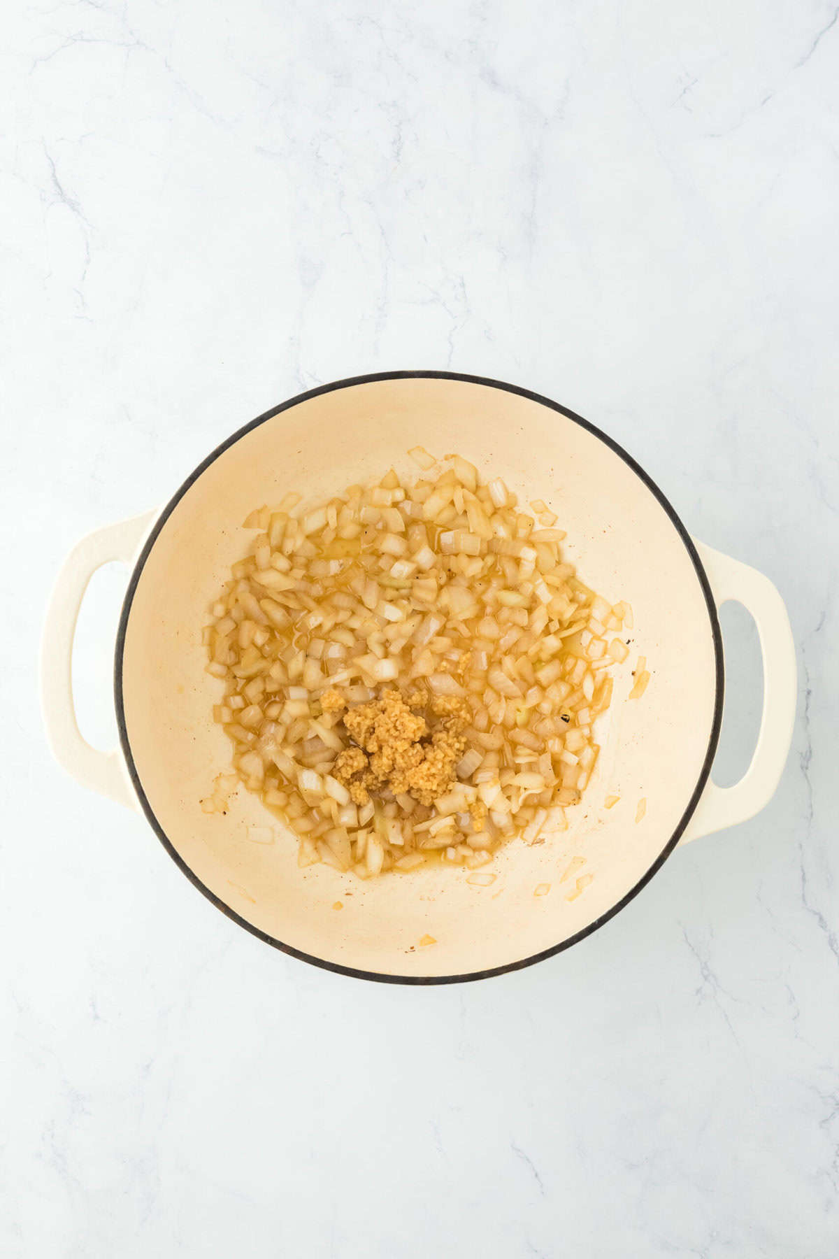 Cooked onion and minced garlic in a dutch oven on white countertop