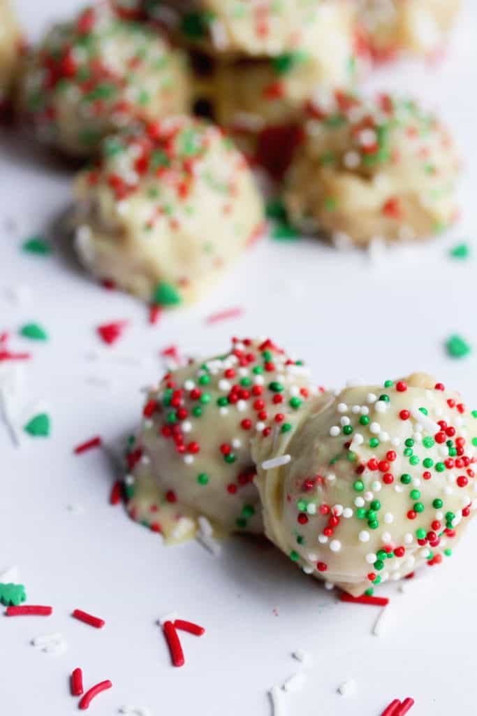 Two Eggnog Cookie Truffles topped with red, green and white sprinkles with more truffles in the background