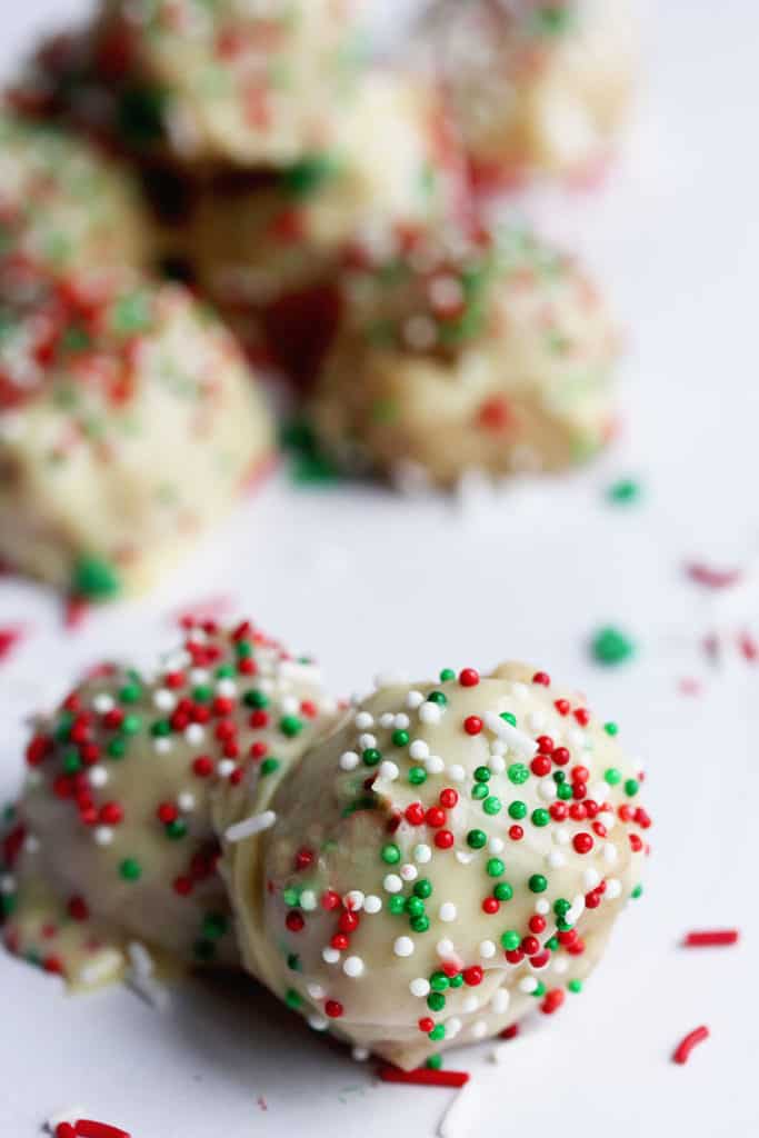 Close up of two Eggnog Cookie Truffles topped with red, green and white sprinkles with more truffles in the background