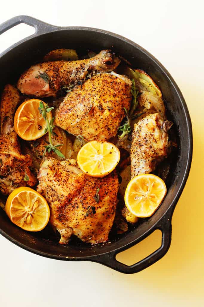 Overhead shot of lemon roast chicken in a cast iron pot with half lemons and potatoes