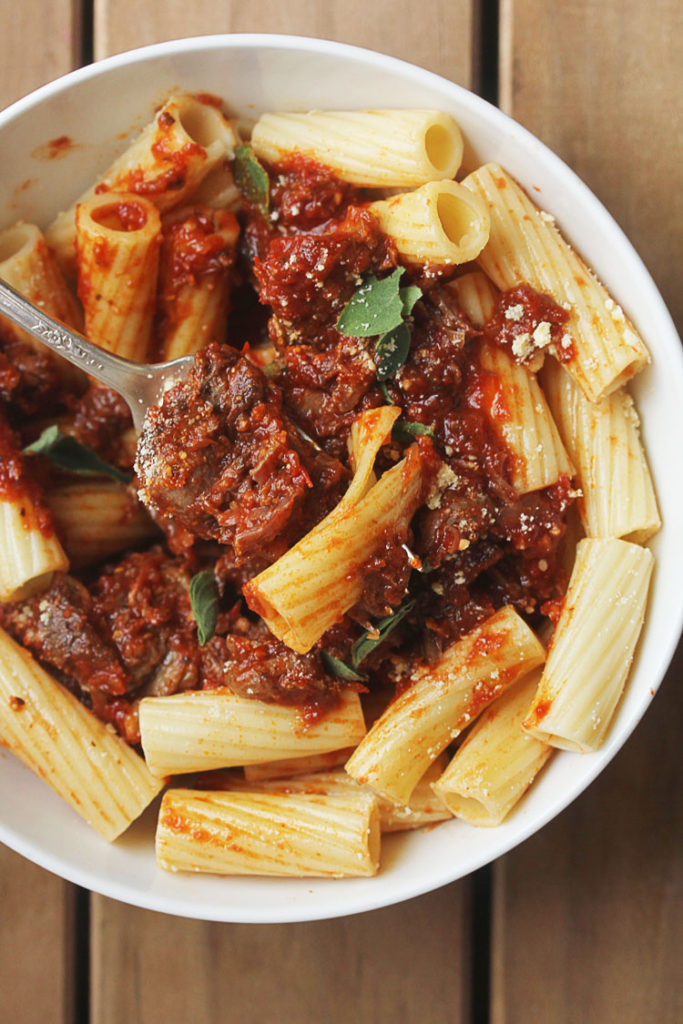 Italian pot roast in thick bolognese sauce recipe and rigatoni ready to eat with fork pierced through pasta