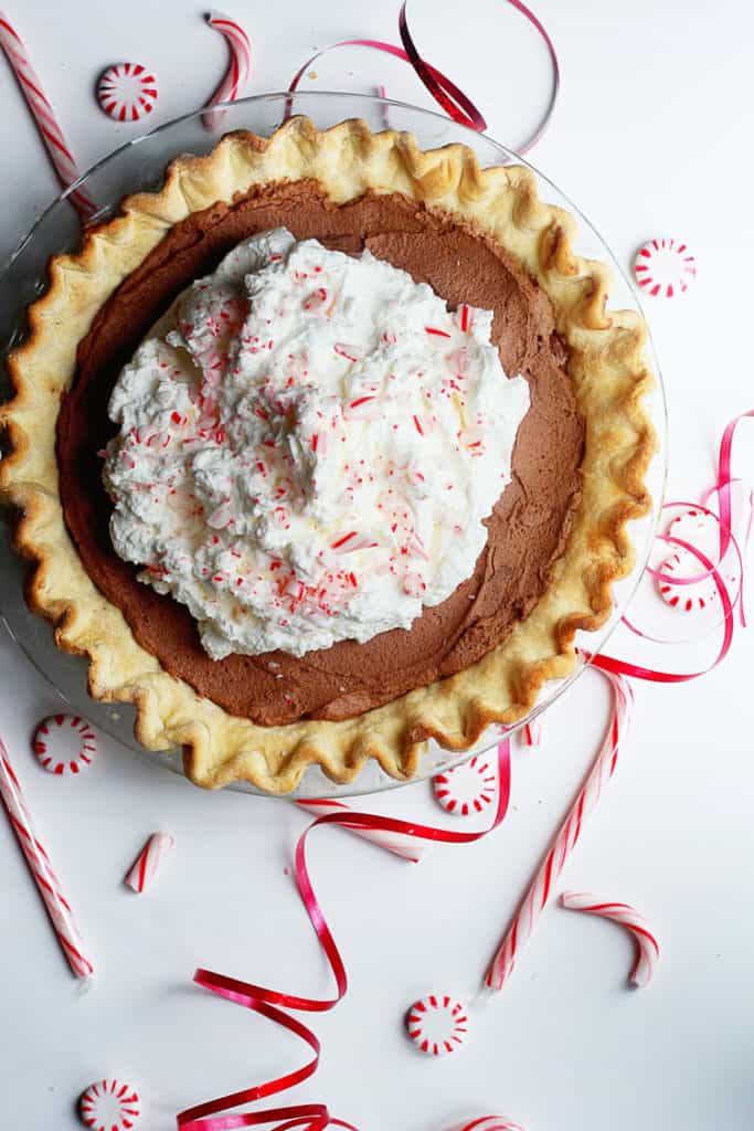 Peppermint French Silk Pie with candy canes and peppermint candy surrounding the transparent plate it sits on.