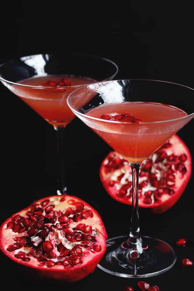 Two glasses of Pomegranate Orange Champagne Cocktail next to two halves of a fresh pomegranate