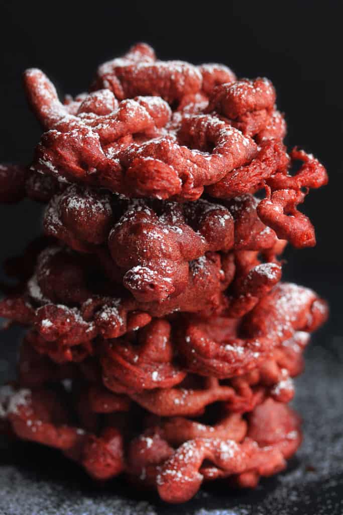 Close up of a stack of red velvet funnel cakes topped powdered sugar