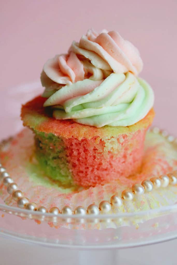 Close up of a pink and green vanilla cupcake with the wrapper removed and a necklace of pearls wrapped around it