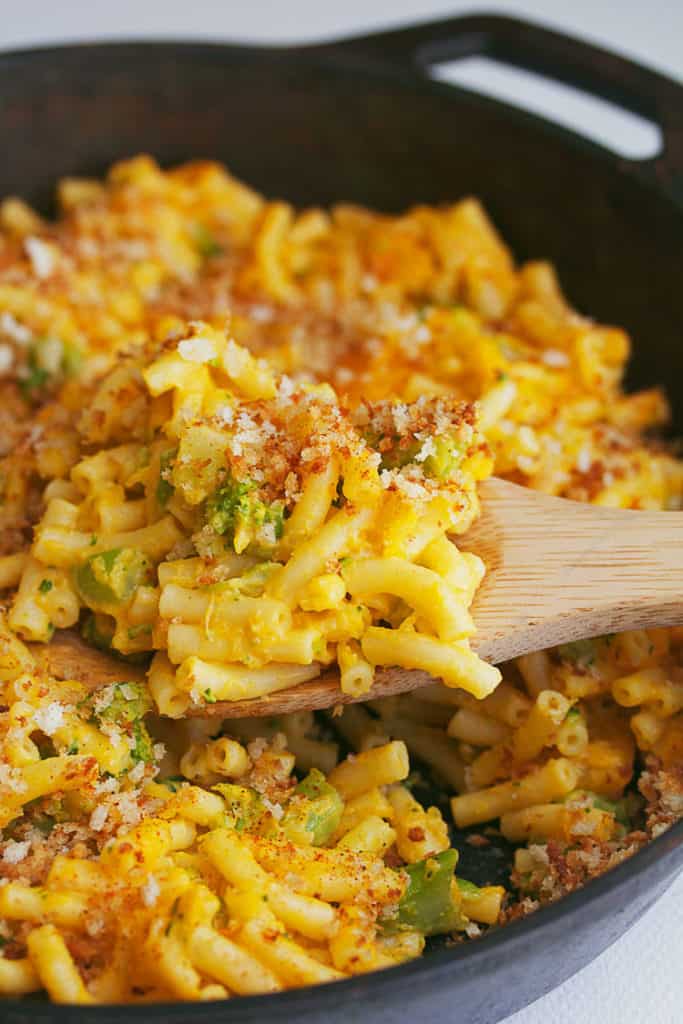 Close up of Butternut Squash Broccoli Mac and Cheese contained in a cast iron skillet with a wooden spoon in it