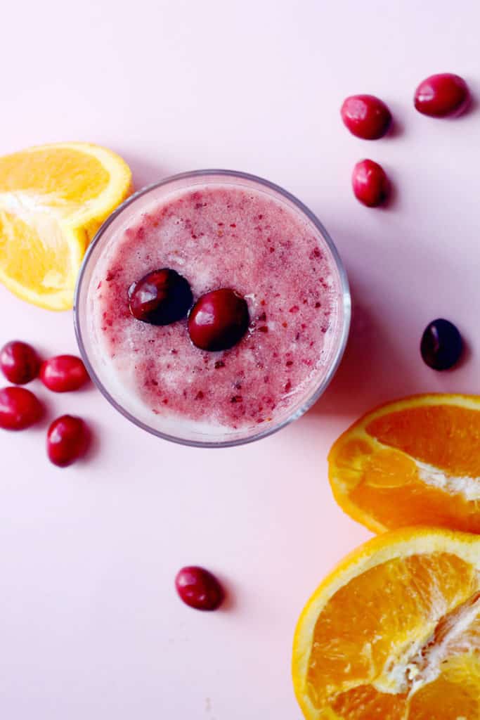 Overhead shot of a cup of Cranberry Orange Smoothie surrounded by orange wedges and fresh cranberries