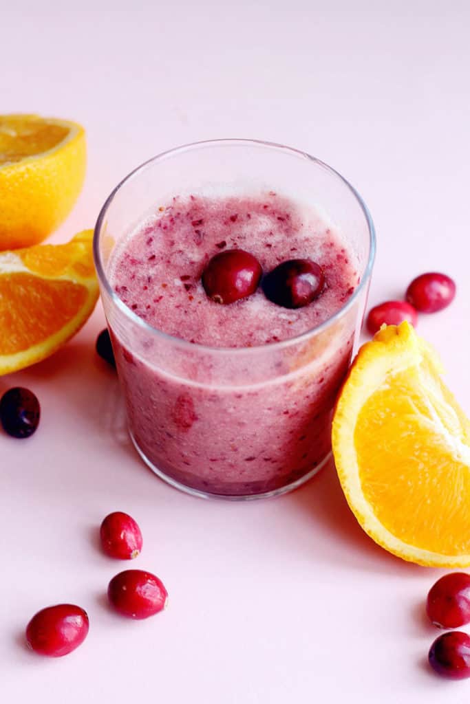 Close up of a cup of Cranberry Orange Smoothie surrounded by orange wedges and fresh cranberries