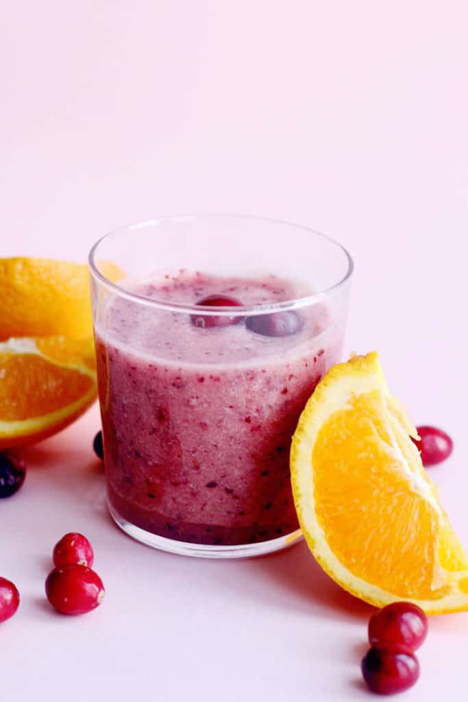 A cup of Cranberry Orange Smoothie surrounded by orange wedges and fresh cranberries