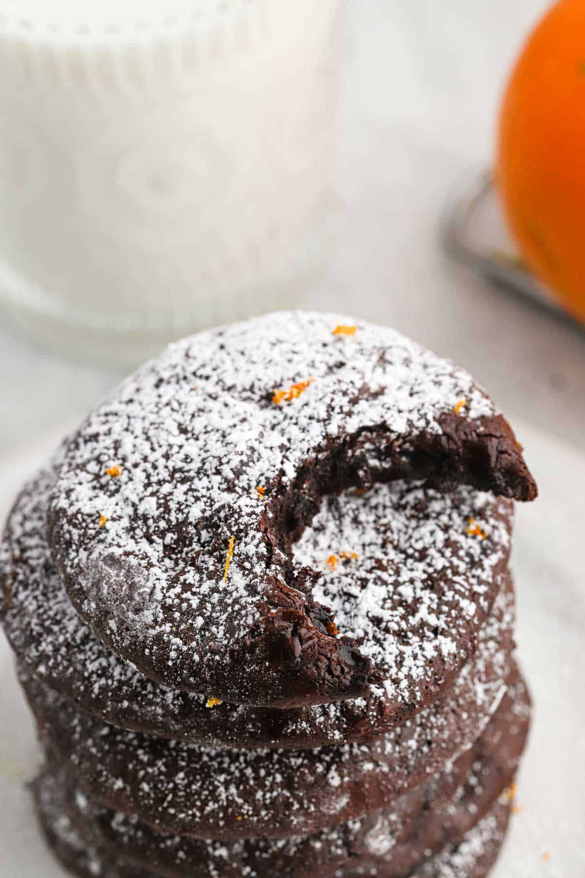Stack of chocolate orange cookies on a plate with a bite missing from the top one and a glass of milk in the background.
