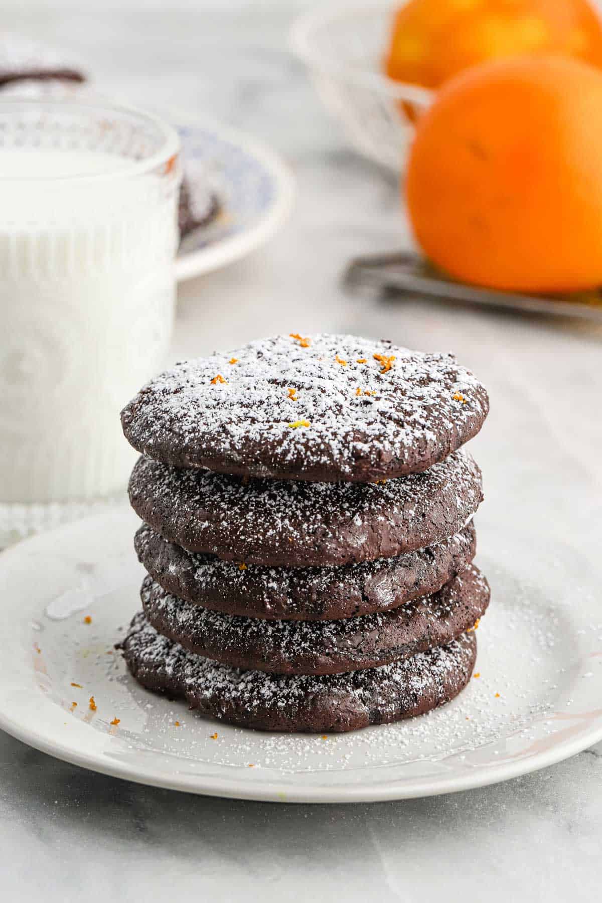 A stack of Flourless Chocolate Orange Cookies displayed on a white plate with oranges slices surrounding it