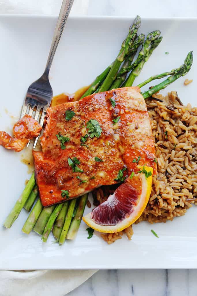 An overhead of orange honey glazed salmon recipe with sauce over rice and asparagus ready to serve with fork