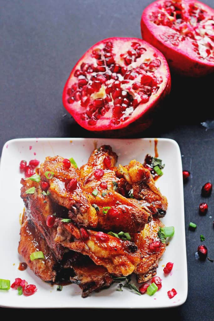 Wings glazed with a pomegranate honey sauce ready to serve on a white plate with a pomegranate cut in half in the background
