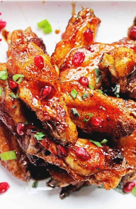 Pomegranate chicken wings piled up on a white plate