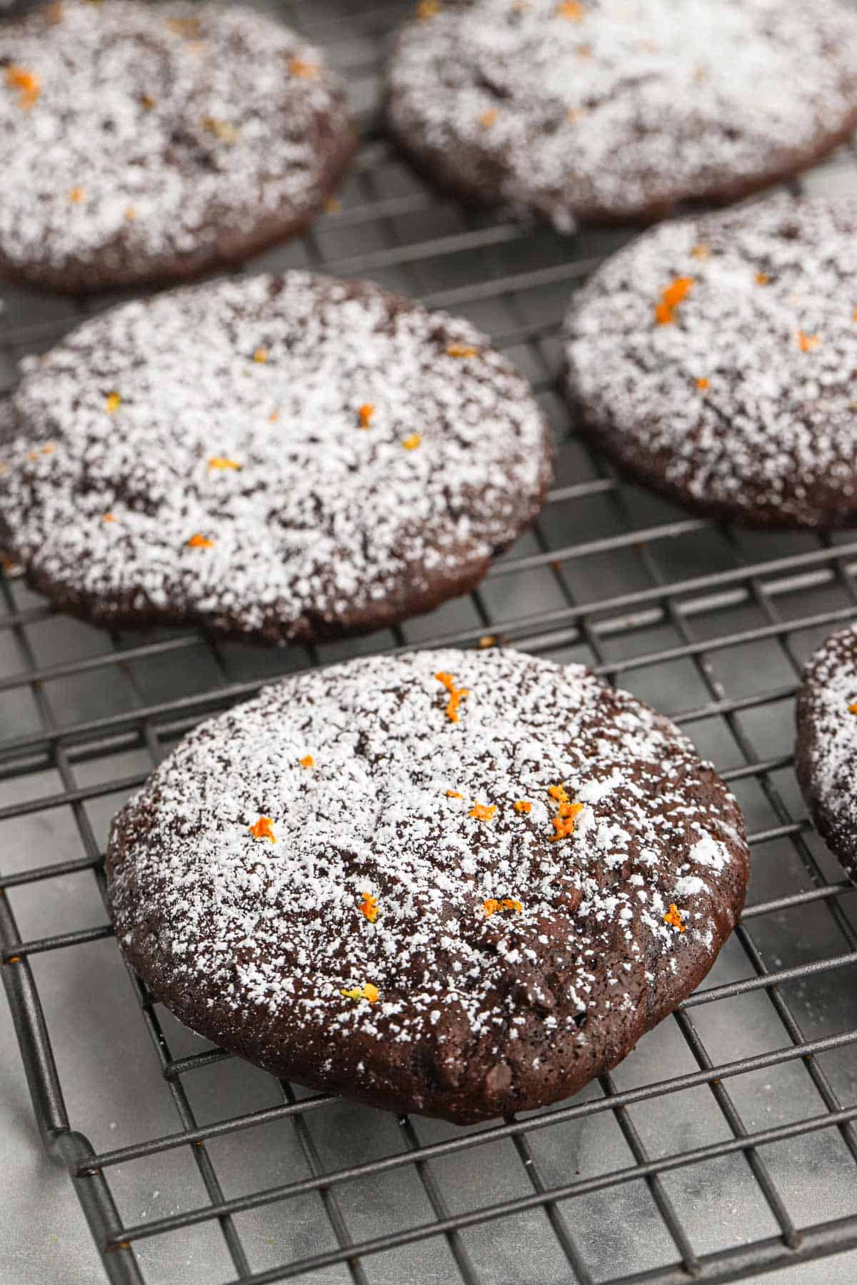 Chocolate orange cookies on a wire rack lightly dusted with powdered sugar.