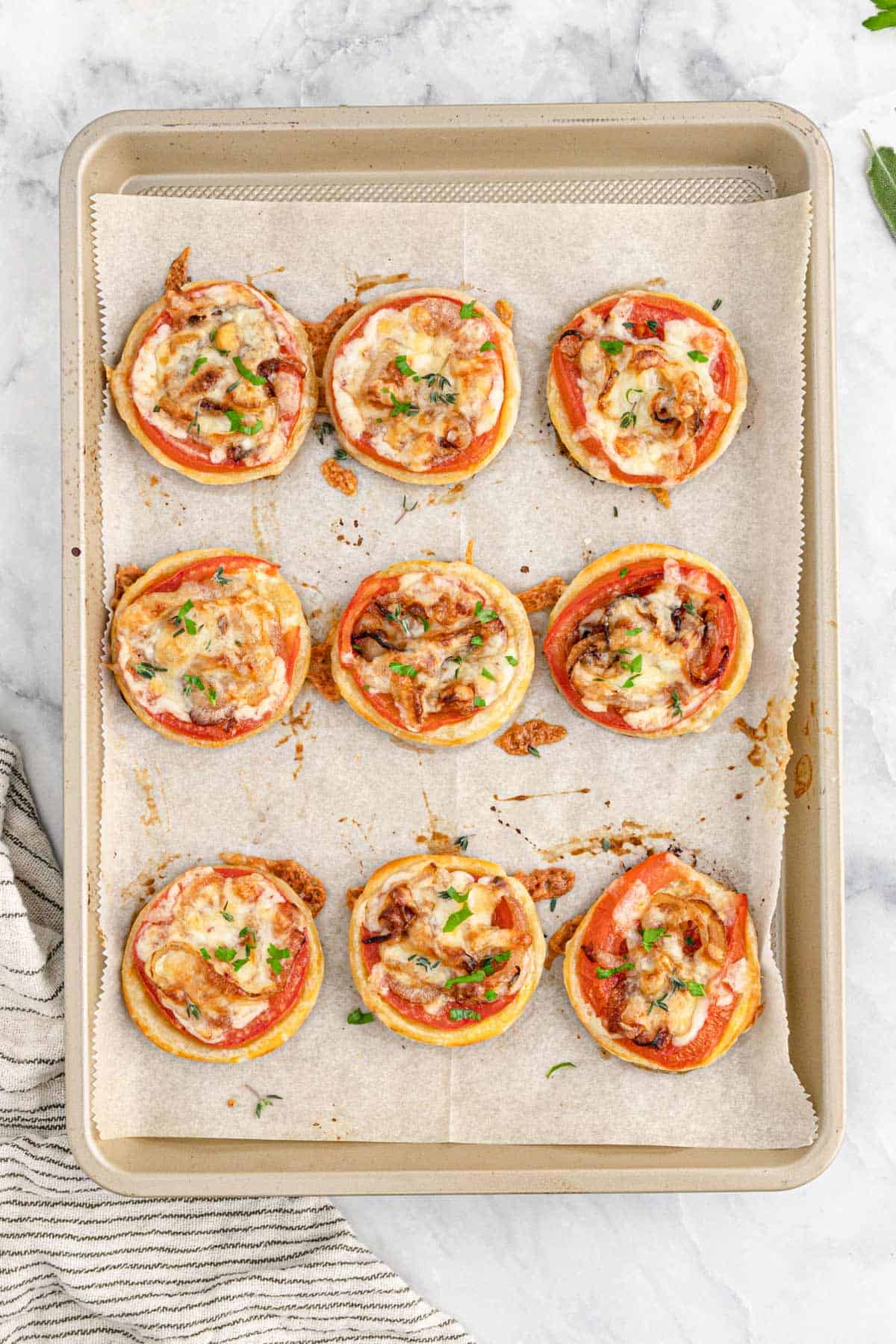 A tray of baked tomato tarts on puff pastry on the table.
