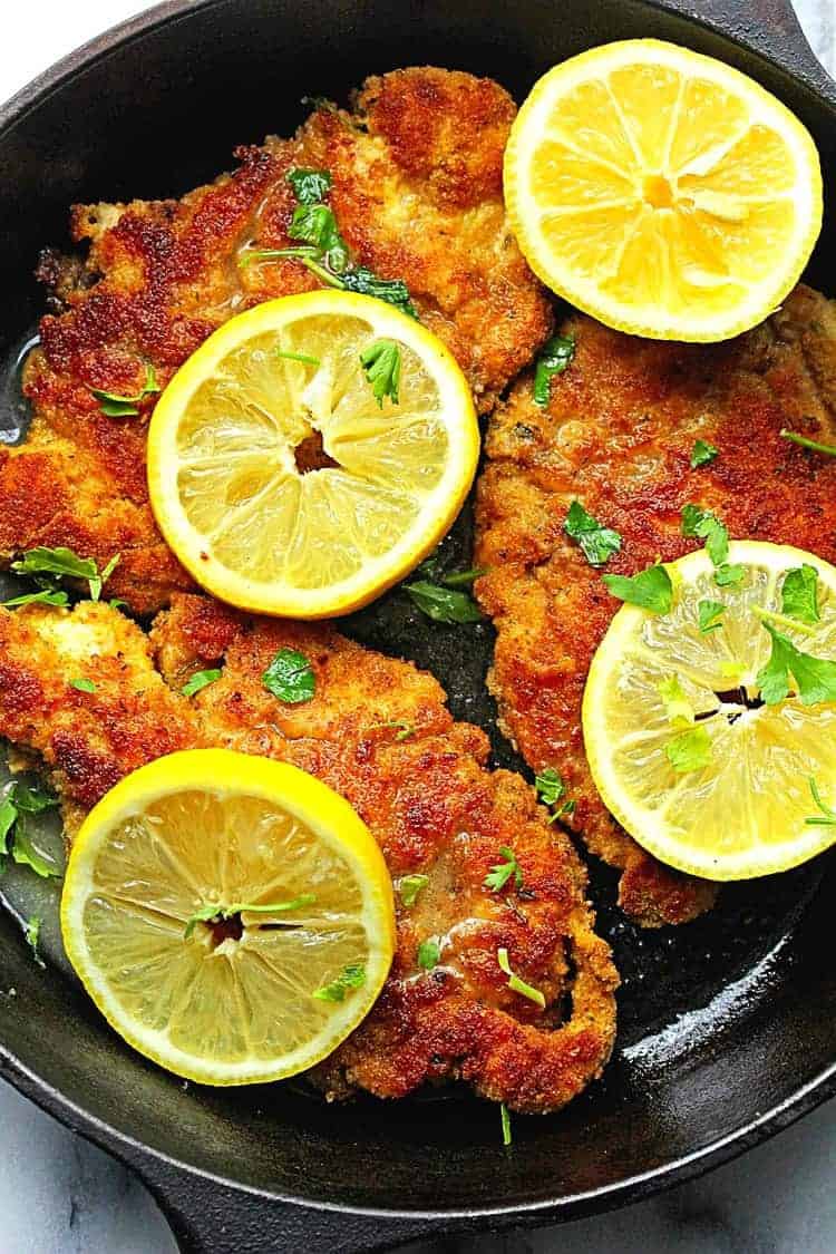 Overhead shot of lemon piccata chicken contained in a black cast iron skillet with lemons