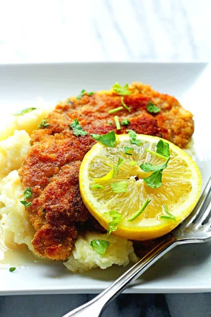 Lemon Chicken Piccata Recipe served on a bed of mashed potatoes with wine sauce and lemon garnish
