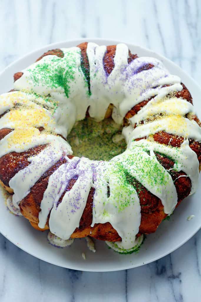 Easy King Cake Recipe topped with cream cheese icing and purple, yellow and green sanding sugar. 