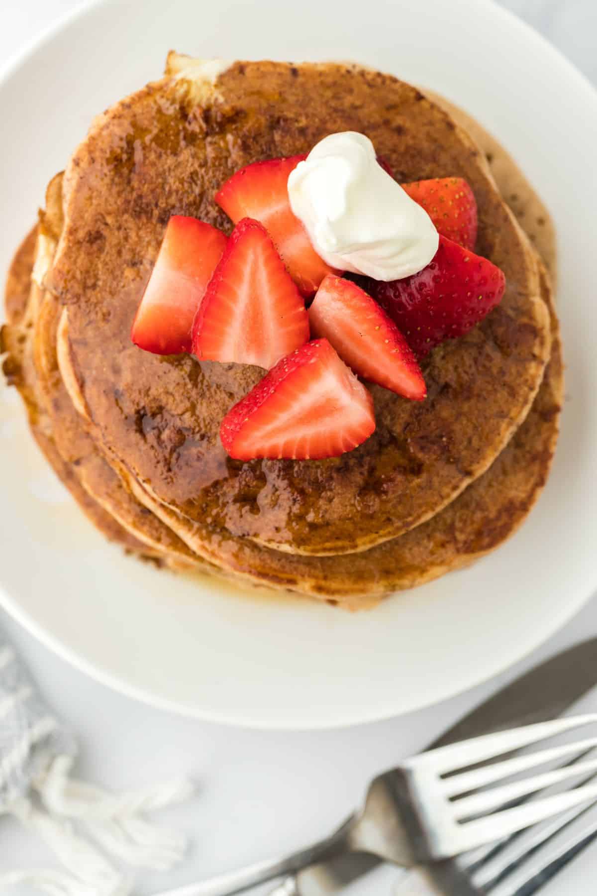 A stack of french toast pancakes recipe topped with whipped cream and fresh strawberry slices.