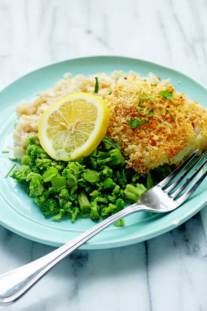 Panko Fish surrounded by rice and broccoli pieces served on a light blue plate with a fork