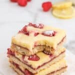 A stack of lemon raspberry bars on the counter with fresh berries and lemon slices.