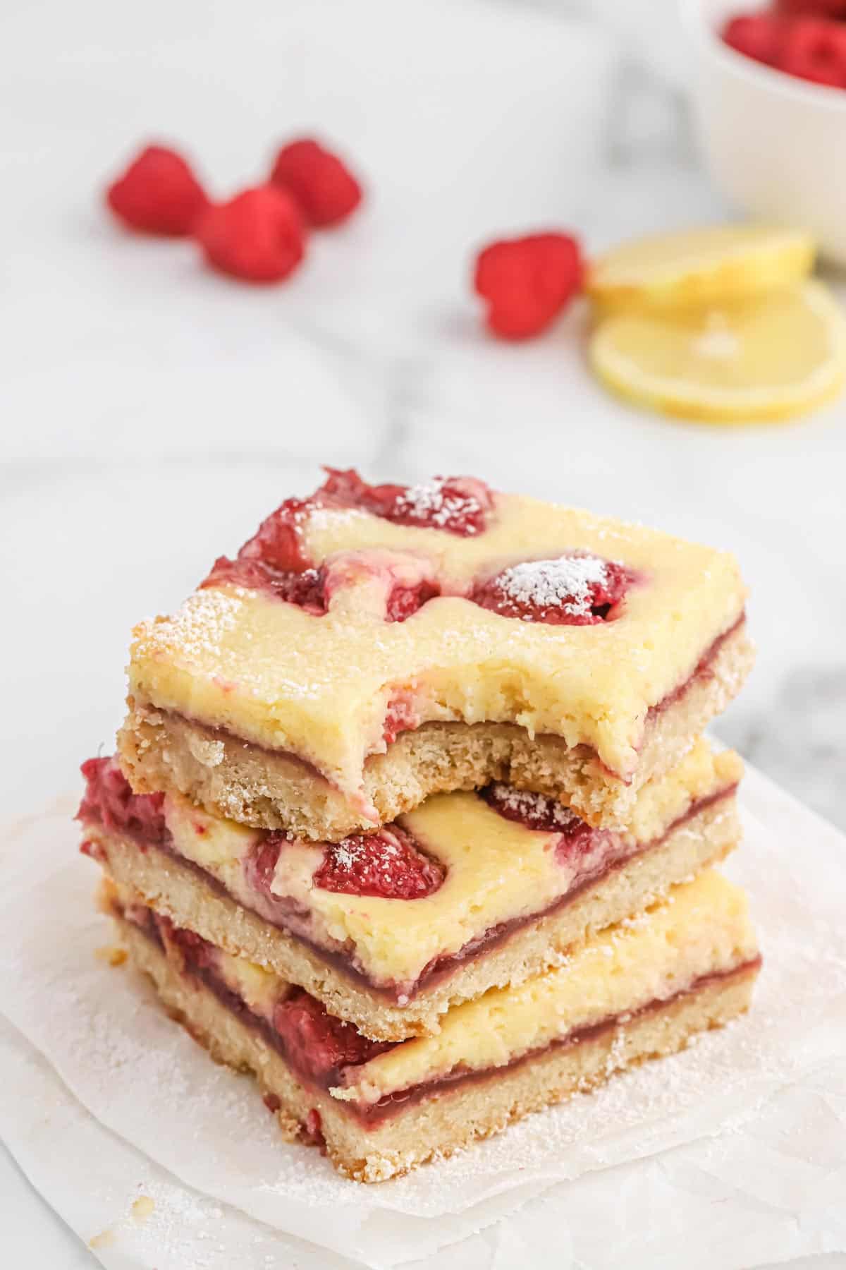 A stack of lemon raspberry bars on the counter with fresh berries and lemon slices.
