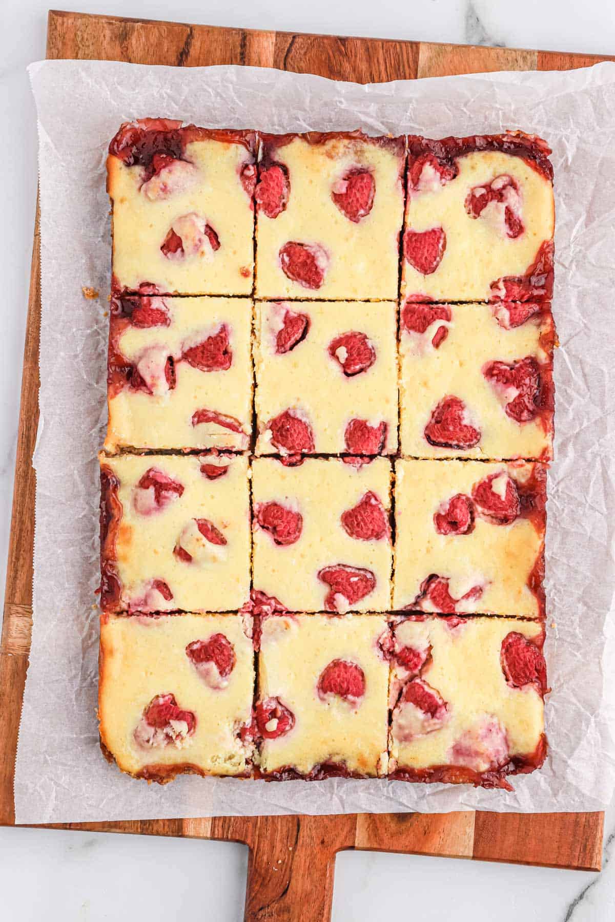 Raspberry lemon bars on a cutting board and parchment cut into squares.