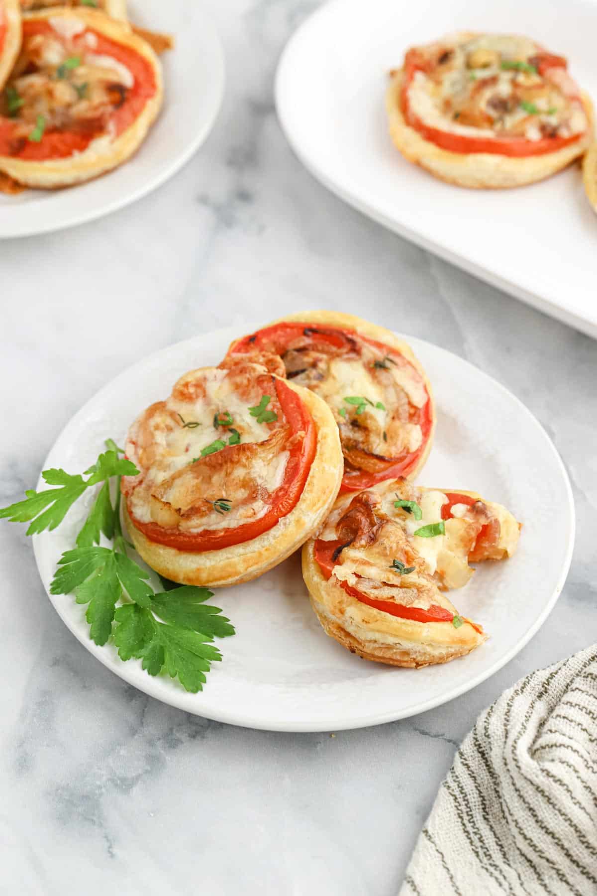 Mini tomato puff pastry tarts on a plate with a piece of parsley.