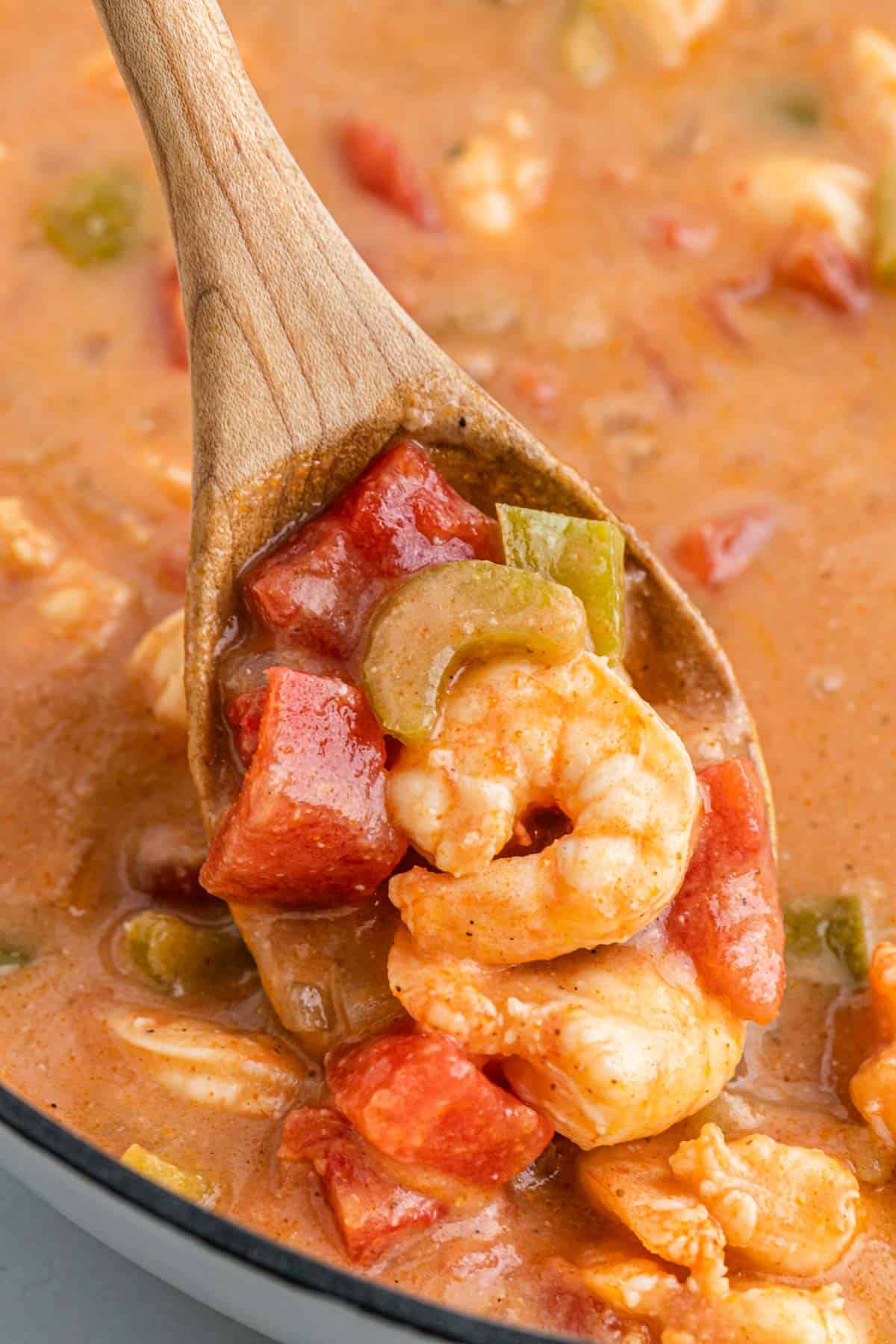 A closeup of shrimp etouffee in a pan with a wooden spoon pulling a bite out.