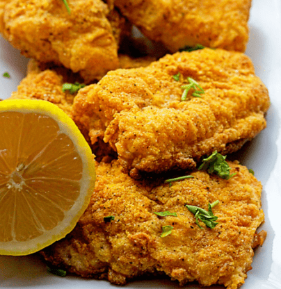 Close up of oven fried catfish fillets with lemon served on a white plate