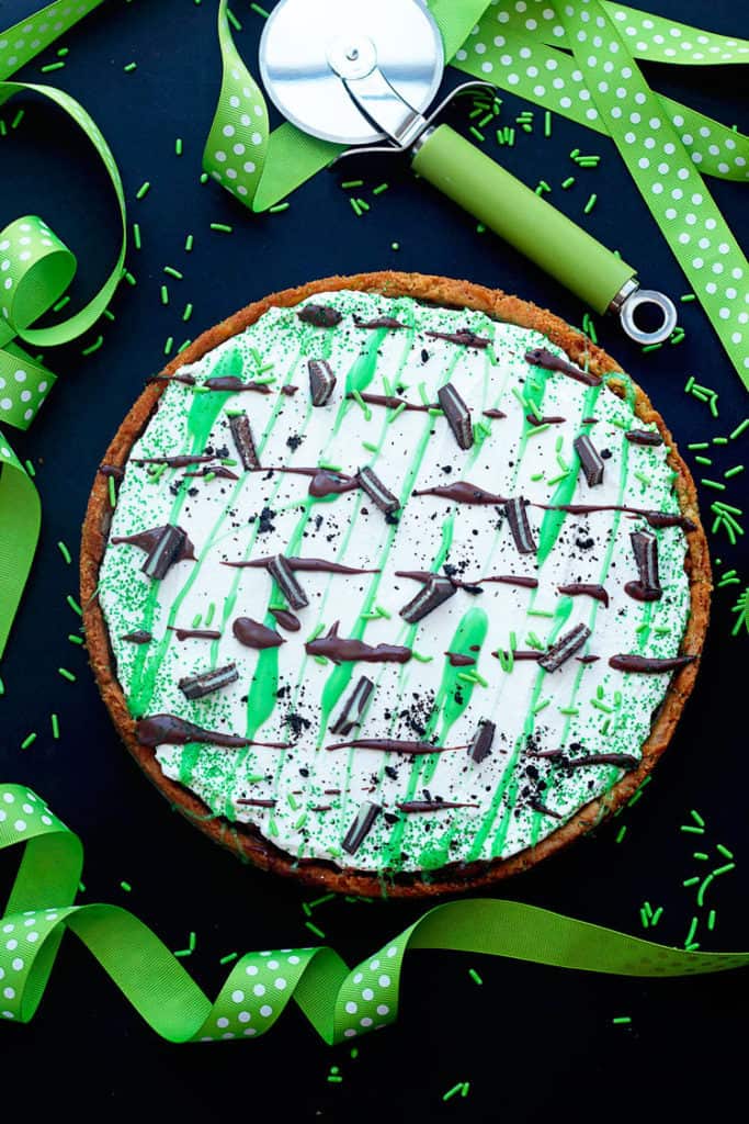 Overhead shot of a St. Patrick's Day Dessert Pizza surrounded by green streamers, green sprinkles and a pizza cutter