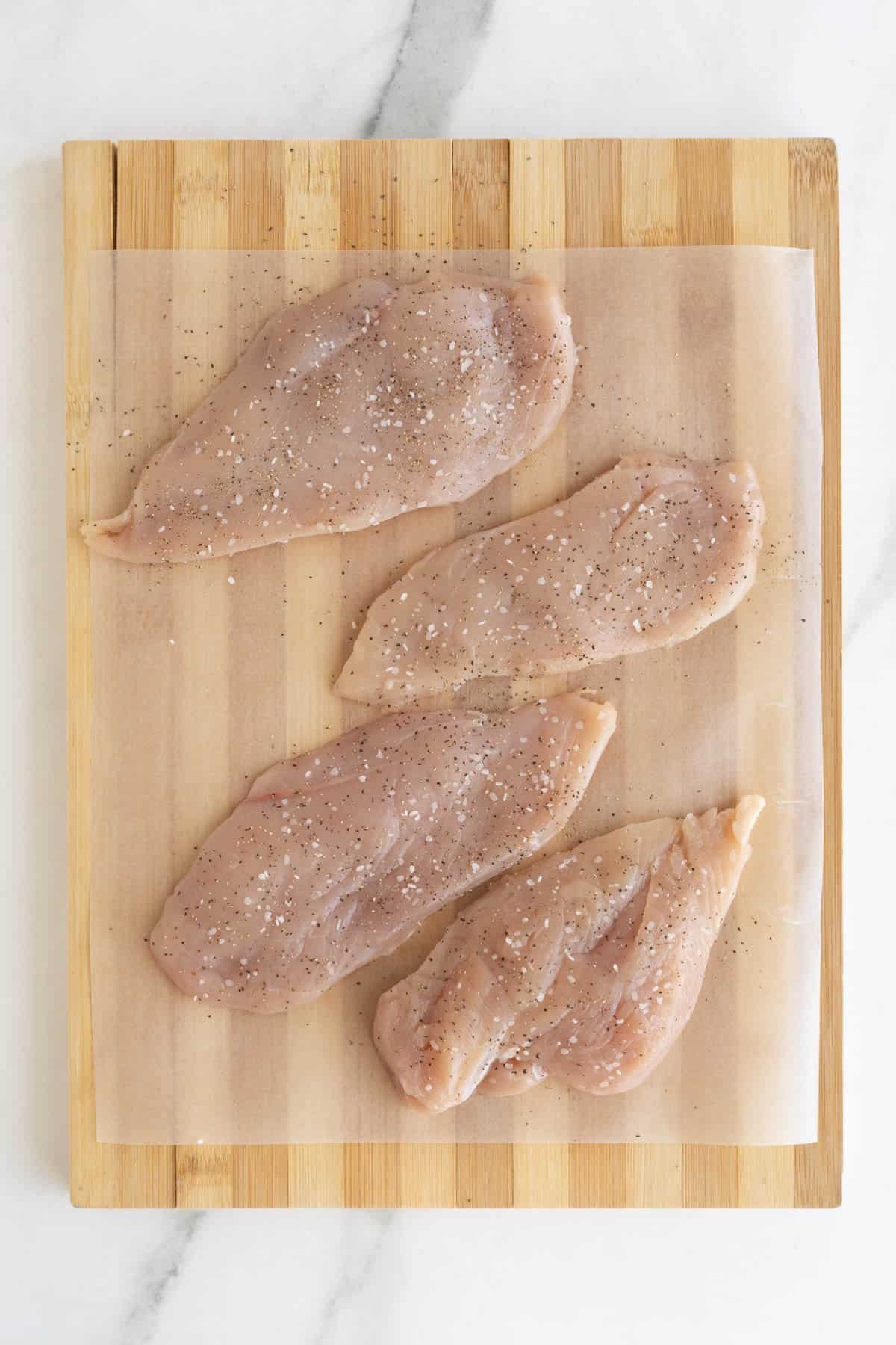 Raw seasoned chicken breasts on parchment paper over a wooden board