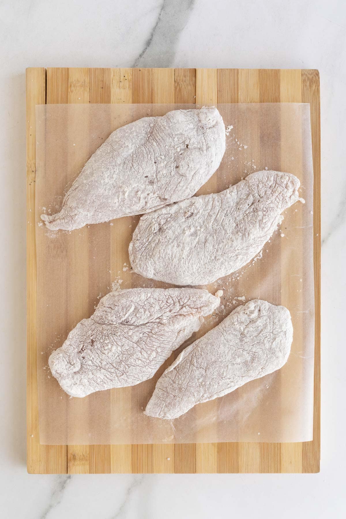 Flour dusted chicken breasts on a wooden board
