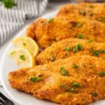 Oven fried fish fillets on a white platter with lemon wedges
