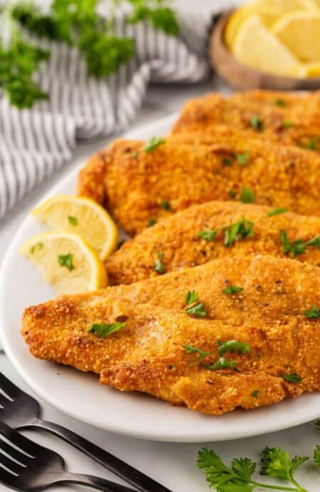Oven fried fish fillets on a white platter with lemon wedges