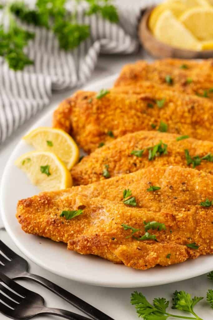 Oven fried fish fillets on a white platter with lemon wedges