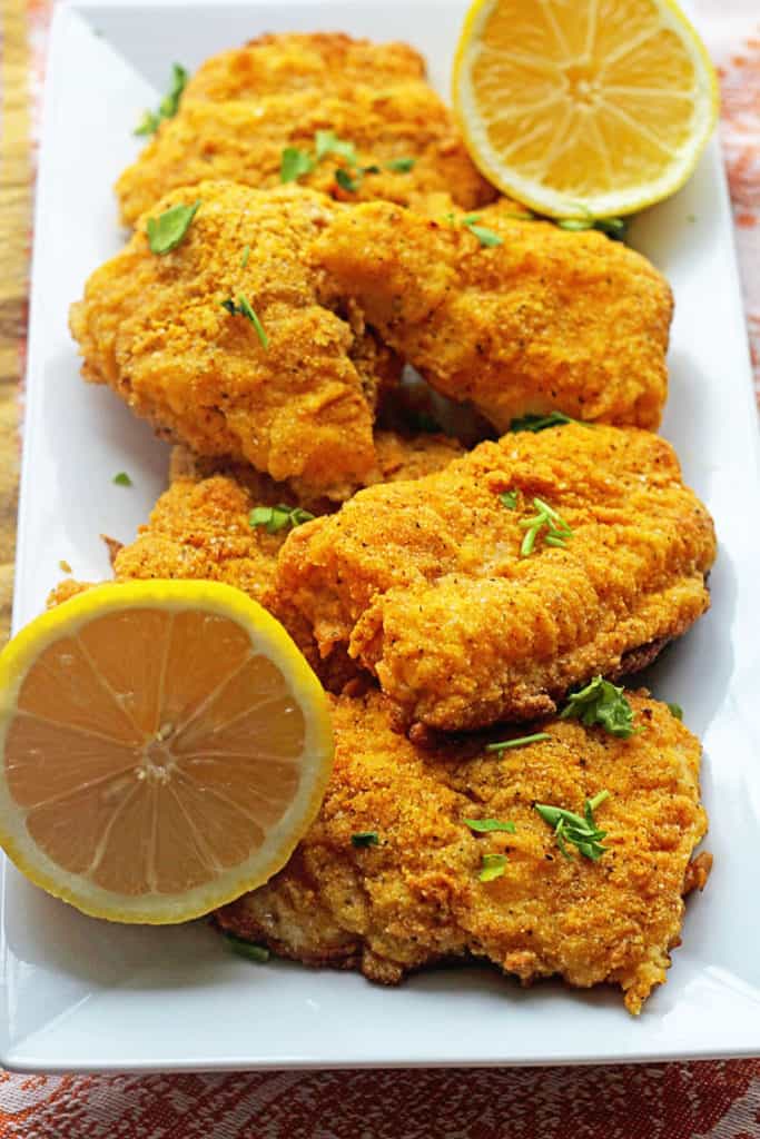 Delicious spicy oven fried catfish fillets sprinkled with parsley and garnished with lemon ready to serve