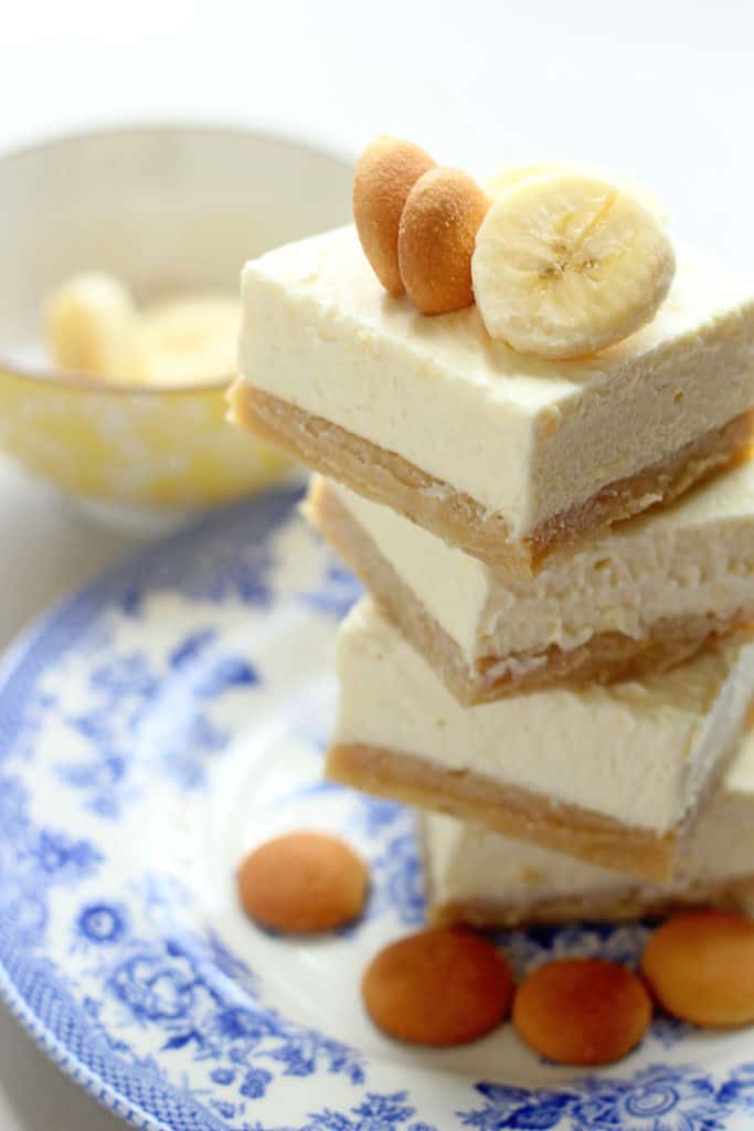 A stack of 4 Banana Pudding Cheesecake Bars on top of white and blue plate with nilla waffer and banana slice garnishes