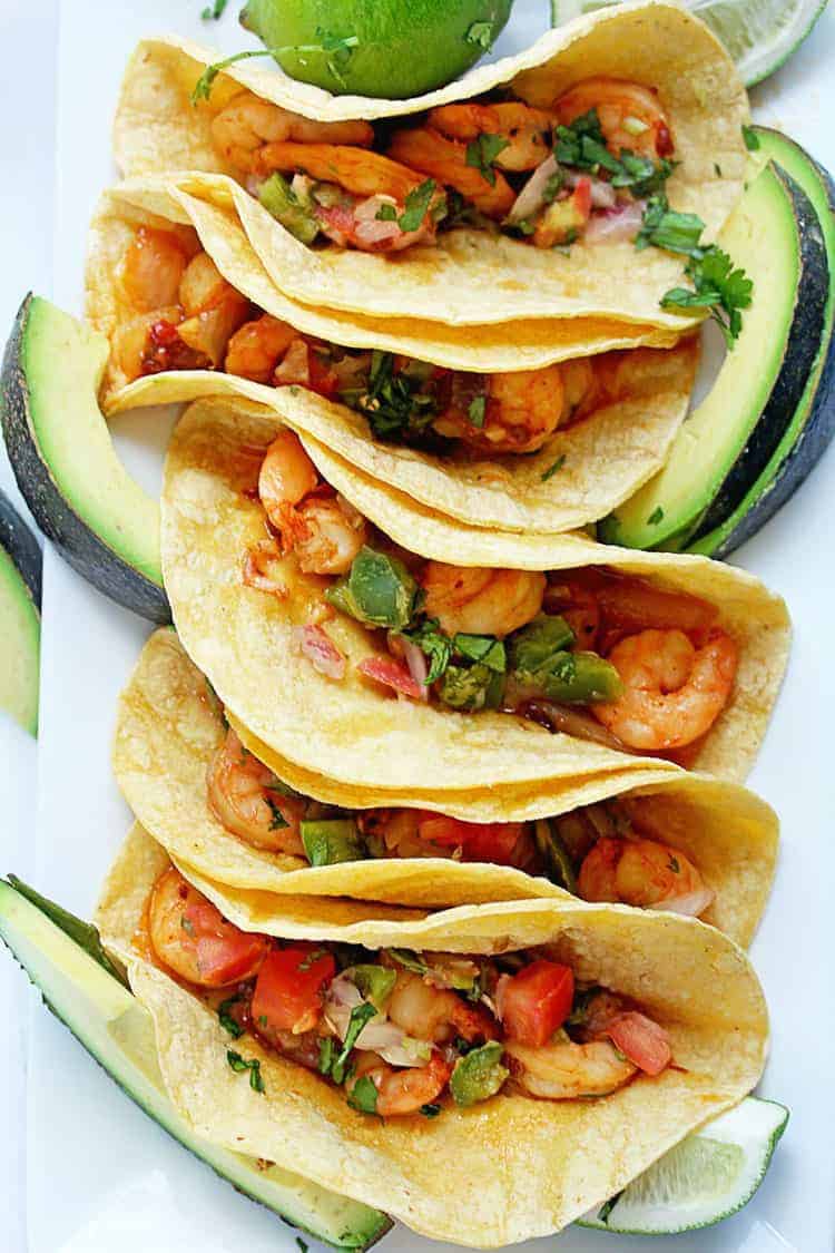 Overhead shot of several chipotle shrimp tacos garnished with cilantro and avocado slices