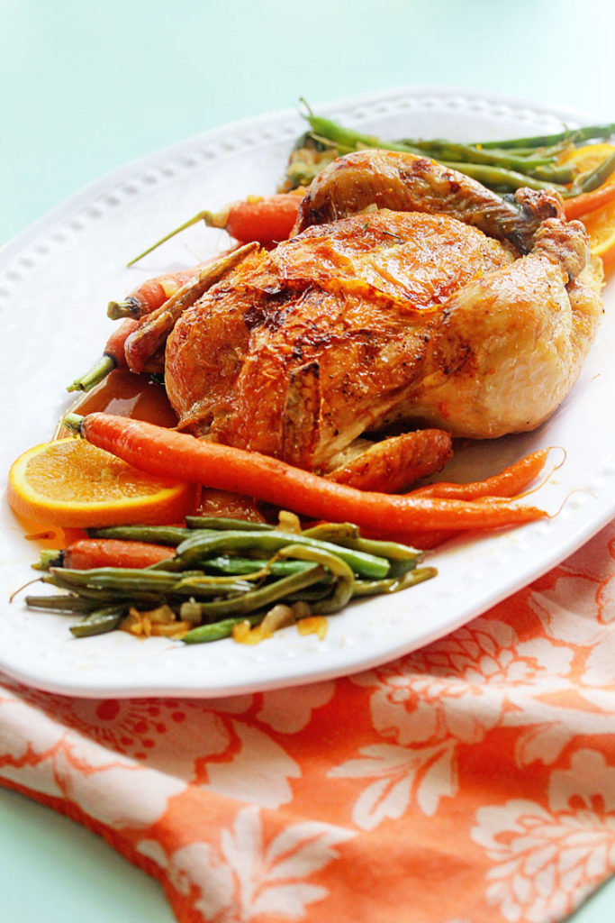 Orange roasted Honey Chicken served on a white tray with green beans, carrots and orange slices