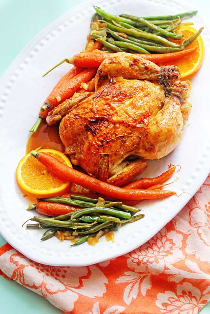 Overhead shot of an Orange Honey Roast Chicken served on a white tray with green beans, carrots and orange slices